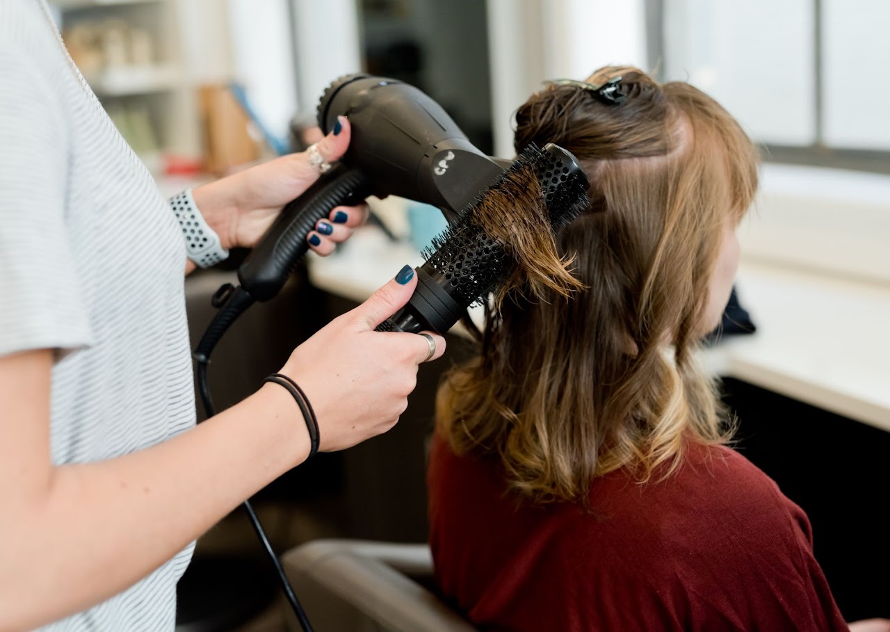 A stylist blow-drying and styling hair with a round brush